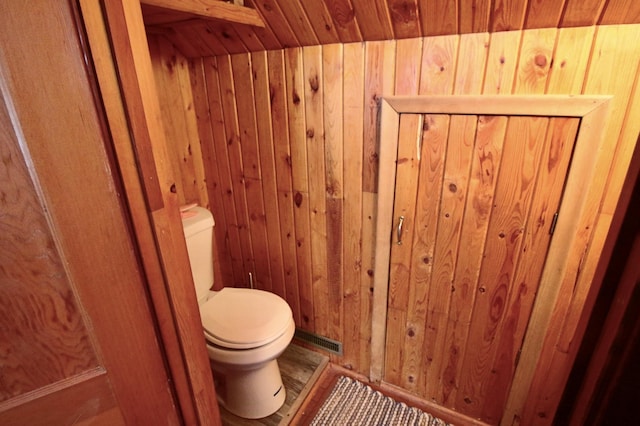 bathroom featuring toilet, wood walls, and visible vents