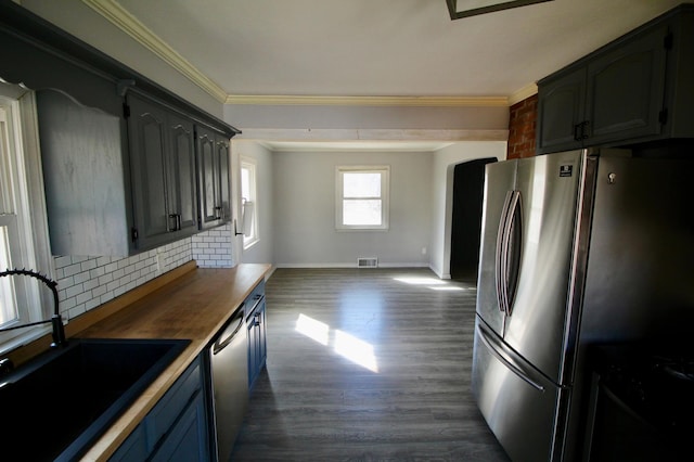 kitchen featuring tasteful backsplash, ornamental molding, dark wood-type flooring, appliances with stainless steel finishes, and a sink