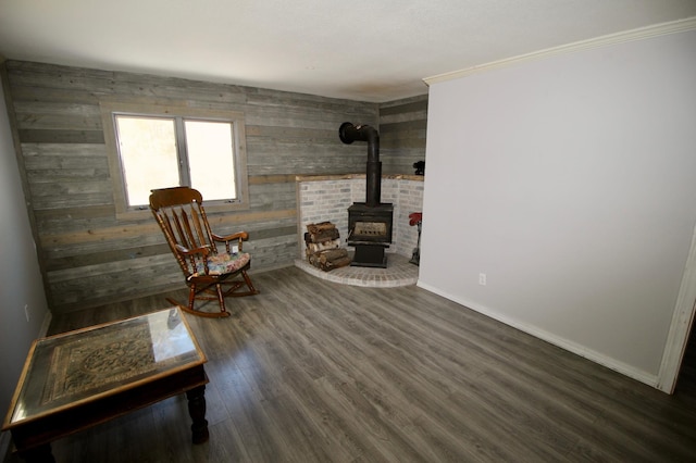 living area with crown molding, a wood stove, wood finished floors, wooden walls, and baseboards