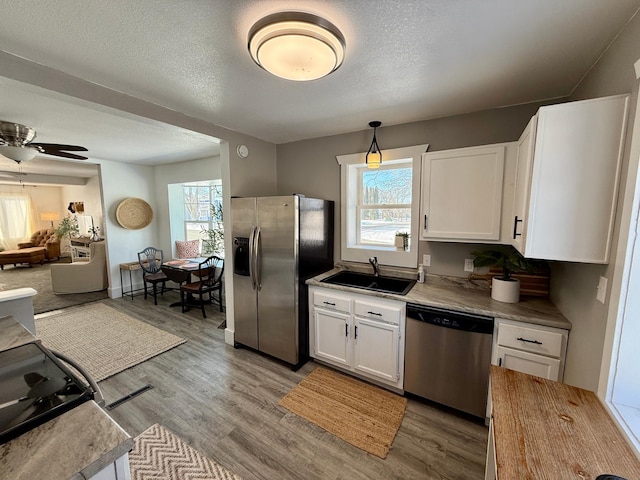 kitchen featuring appliances with stainless steel finishes, sink, light wood-type flooring, white cabinetry, and decorative light fixtures