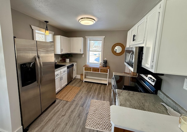 kitchen featuring stainless steel appliances, a textured ceiling, pendant lighting, hardwood / wood-style floors, and white cabinetry