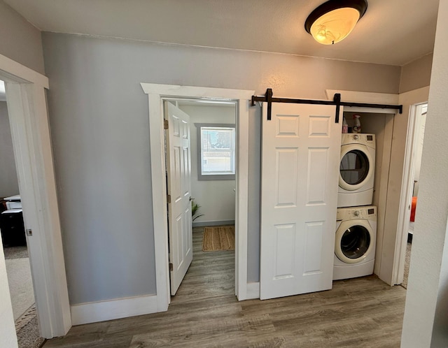 washroom featuring a barn door, stacked washer / drying machine, and wood-type flooring