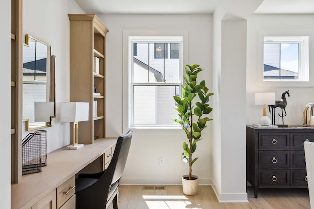 office area with a wealth of natural light, built in desk, and light hardwood / wood-style floors