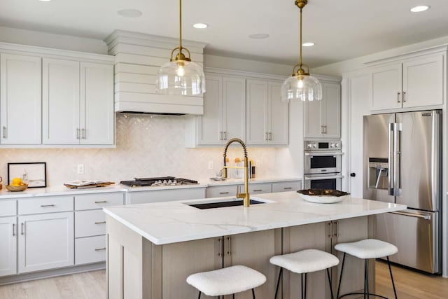 kitchen with an island with sink, sink, white cabinets, stainless steel appliances, and light stone countertops