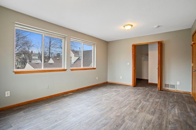 unfurnished bedroom with dark wood-type flooring, a textured ceiling, a closet, and a spacious closet