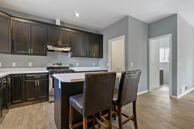 kitchen featuring stainless steel range oven, dark brown cabinetry, light hardwood / wood-style floors, a breakfast bar, and a center island