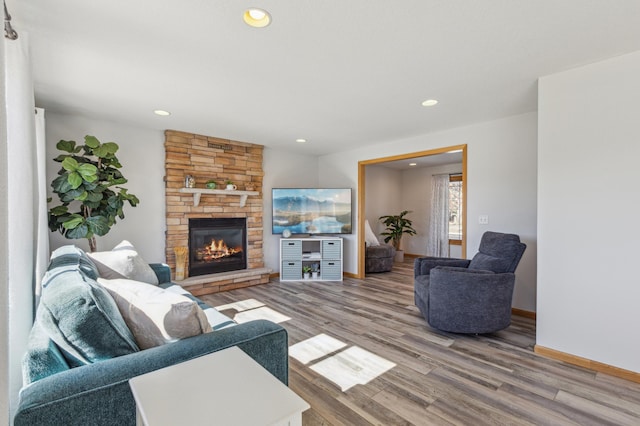 living area featuring a stone fireplace, recessed lighting, baseboards, and wood finished floors