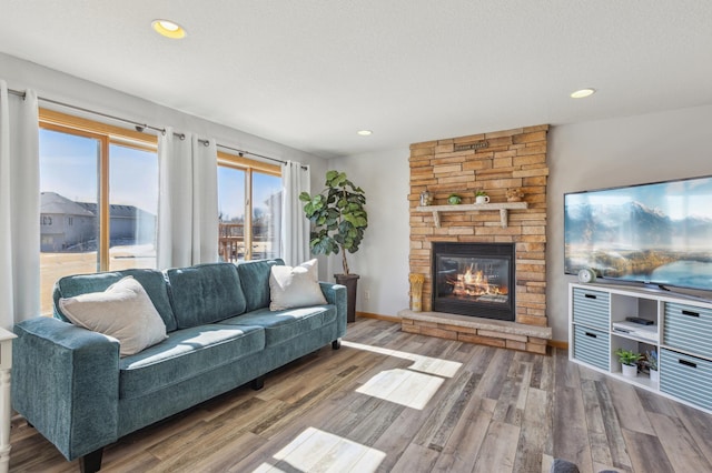 living room with a textured ceiling, wood finished floors, recessed lighting, a stone fireplace, and baseboards