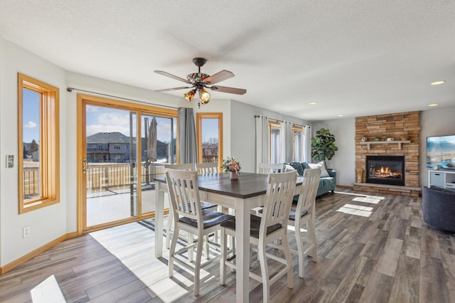 dining space with wood finished floors, baseboards, recessed lighting, a stone fireplace, and a textured ceiling