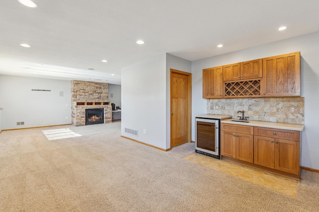 kitchen featuring beverage cooler, visible vents, a sink, backsplash, and a large fireplace