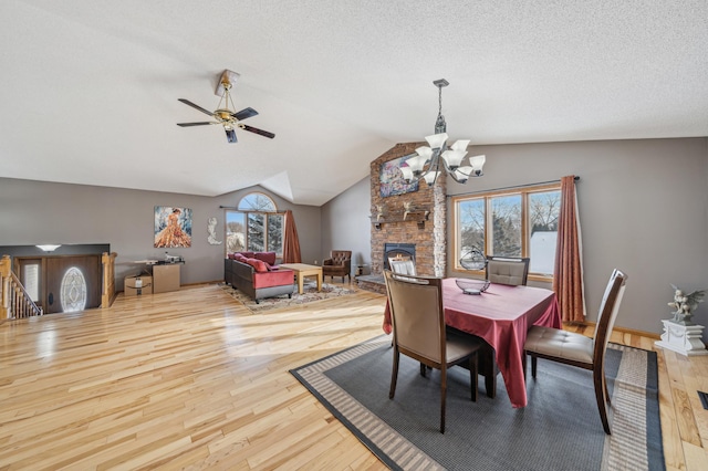 dining area featuring light wood-style floors, vaulted ceiling, a fireplace, and a textured ceiling