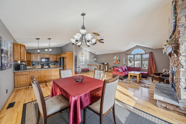 dining room featuring visible vents, vaulted ceiling, a stone fireplace, light wood-type flooring, and a chandelier