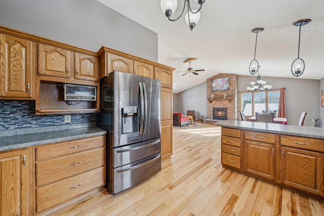 kitchen featuring decorative light fixtures, light wood finished floors, lofted ceiling, dark countertops, and stainless steel fridge