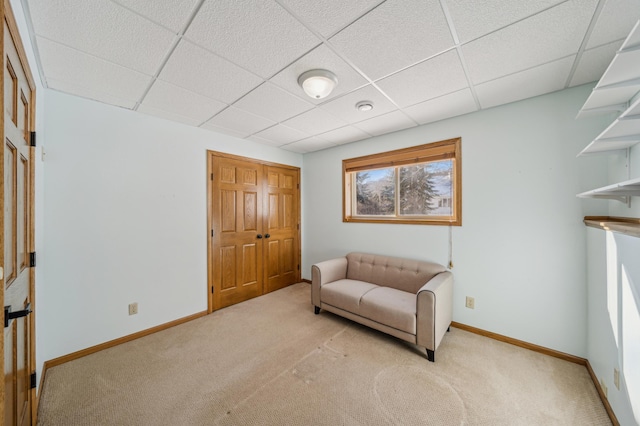 living area featuring a paneled ceiling, light carpet, and baseboards