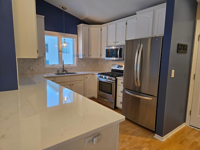 kitchen with appliances with stainless steel finishes, decorative light fixtures, white cabinetry, sink, and light wood-type flooring