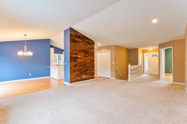 unfurnished living room featuring lofted ceiling, recessed lighting, an inviting chandelier, light carpet, and baseboards