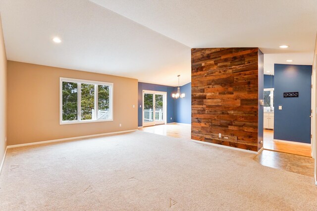 unfurnished living room featuring a notable chandelier, baseboards, light colored carpet, and wooden walls