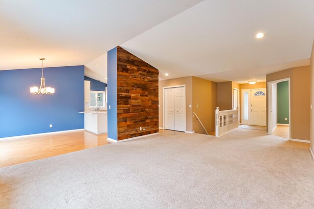 unfurnished living room featuring light carpet, a notable chandelier, baseboards, and lofted ceiling