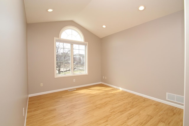 spare room with visible vents, light wood-style flooring, vaulted ceiling, and baseboards