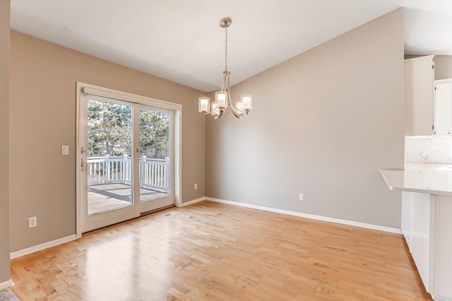 unfurnished dining area featuring light wood-style flooring, vaulted ceiling, an inviting chandelier, and baseboards