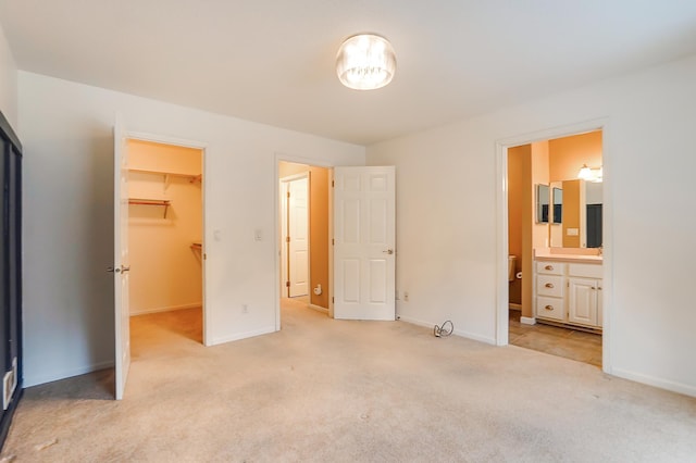 unfurnished bedroom with a closet, baseboards, a spacious closet, carpet, and ensuite bath