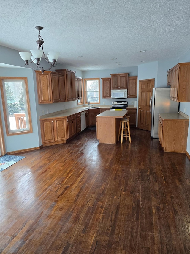 kitchen with a kitchen island, appliances with stainless steel finishes, sink, hanging light fixtures, and dark wood-type flooring