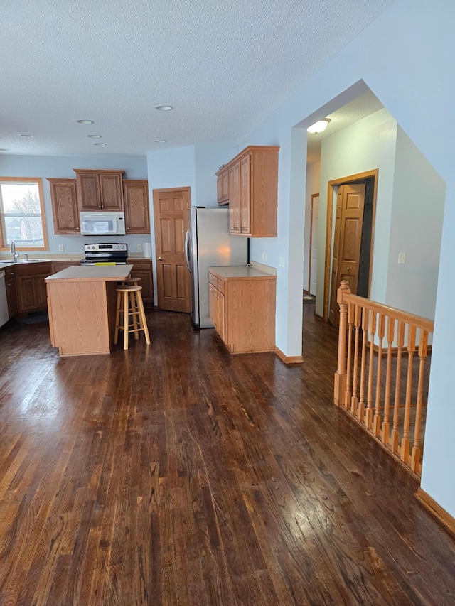 kitchen with sink, a breakfast bar, stainless steel appliances, dark hardwood / wood-style floors, and a kitchen island