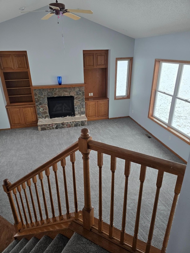 living room featuring lofted ceiling, ceiling fan, carpet floors, a textured ceiling, and a stone fireplace