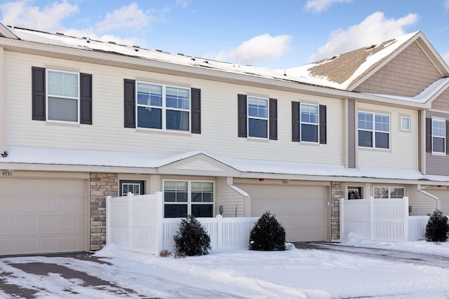 multi unit property with stone siding, an attached garage, and fence