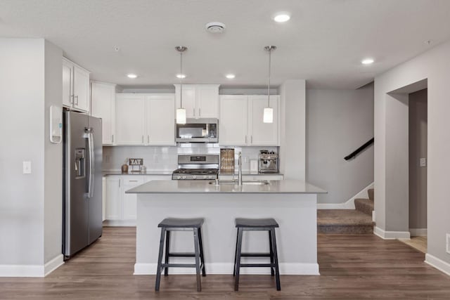 kitchen with a kitchen island with sink, white cabinetry, stainless steel appliances, and decorative light fixtures