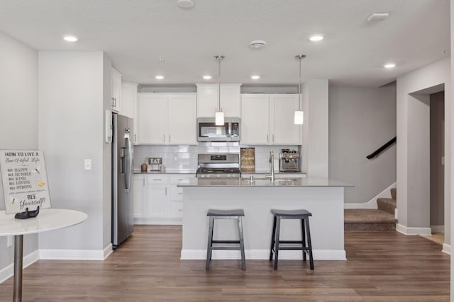 kitchen featuring appliances with stainless steel finishes, pendant lighting, white cabinetry, and a center island with sink