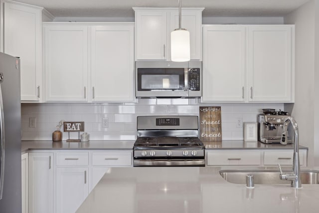 kitchen with pendant lighting, stainless steel appliances, decorative backsplash, white cabinetry, and a sink