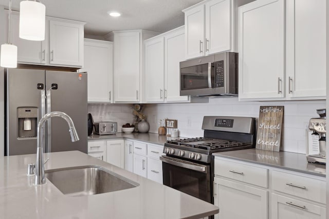 kitchen featuring white cabinets, appliances with stainless steel finishes, decorative light fixtures, light countertops, and a sink