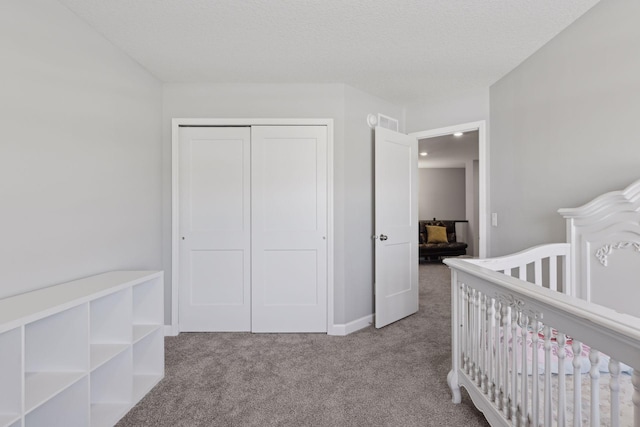 carpeted bedroom featuring a nursery area, a closet, and a textured ceiling