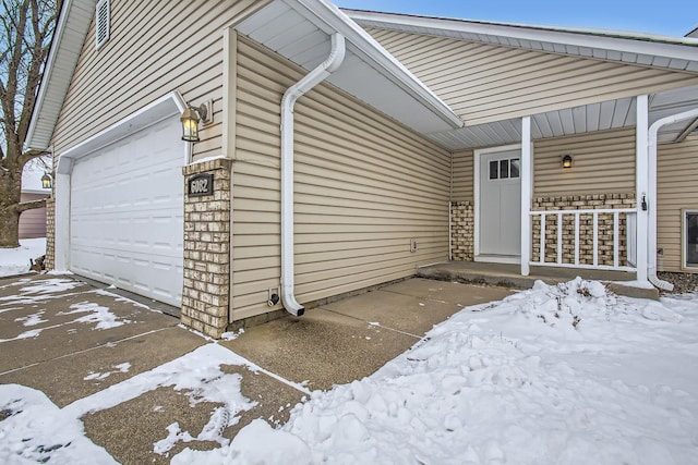 view of snowy exterior with a garage and covered porch