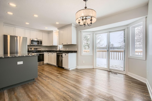 kitchen with pendant lighting, sink, white cabinetry, stainless steel appliances, and dark stone counters