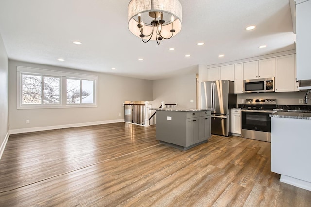 kitchen with appliances with stainless steel finishes, wood-type flooring, white cabinets, dark stone counters, and a center island