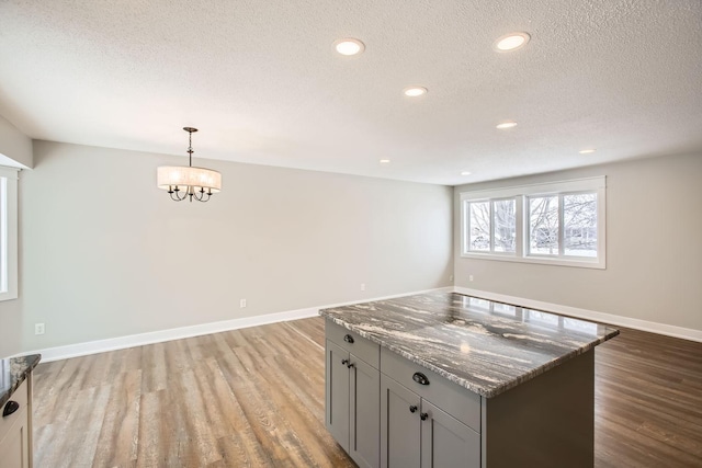 kitchen featuring decorative light fixtures, gray cabinetry, dark stone countertops, a textured ceiling, and light hardwood / wood-style flooring