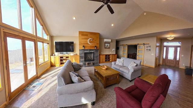 living area featuring high vaulted ceiling, hardwood / wood-style flooring, a barn door, a fireplace, and ceiling fan