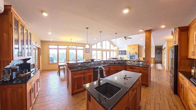 kitchen with black appliances, a kitchen island with sink, a sink, light wood-style floors, and brown cabinetry