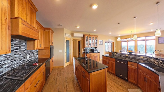 kitchen featuring brown cabinets, black appliances, a center island with sink, a sink, and backsplash