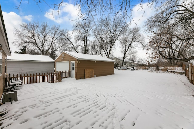 snowy yard with an outdoor structure, a detached garage, and fence