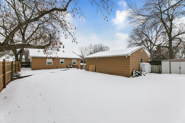 snow covered house featuring a storage shed, a detached garage, fence, and an outdoor structure