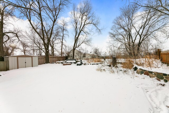 snowy yard featuring an outbuilding, a shed, and fence