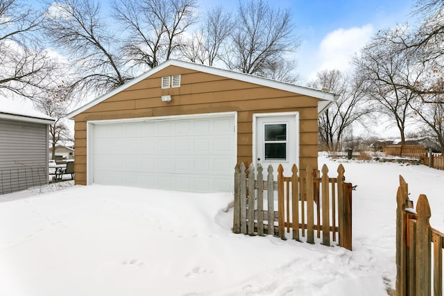 snow covered garage featuring a detached garage and fence