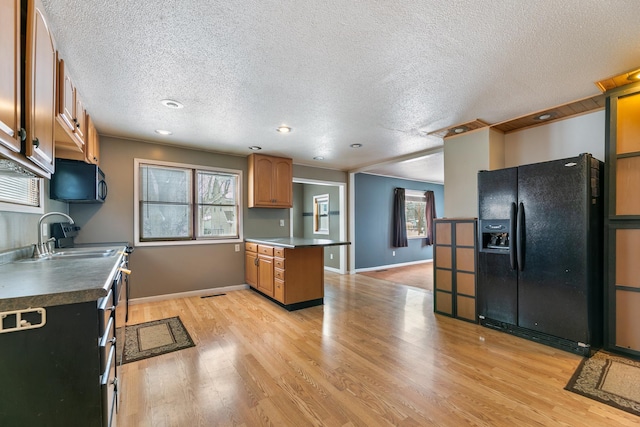 kitchen with stainless steel microwave, a sink, black fridge with ice dispenser, light wood finished floors, and brown cabinetry