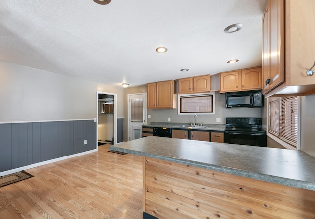 kitchen featuring a wainscoted wall, a sink, light wood-type flooring, black appliances, and dark countertops