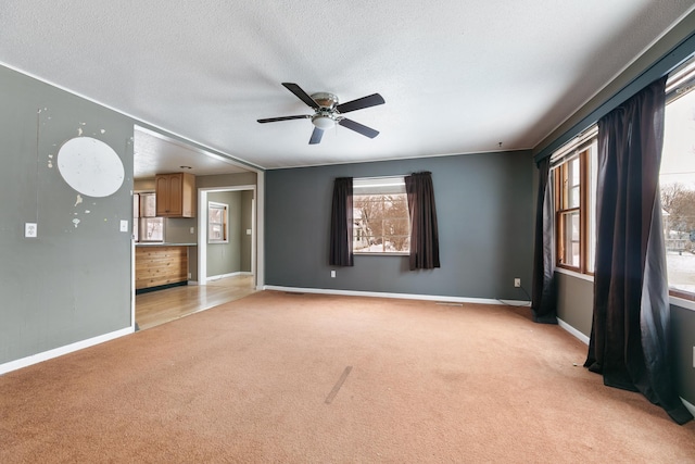 unfurnished living room featuring light colored carpet, ceiling fan, a textured ceiling, and baseboards