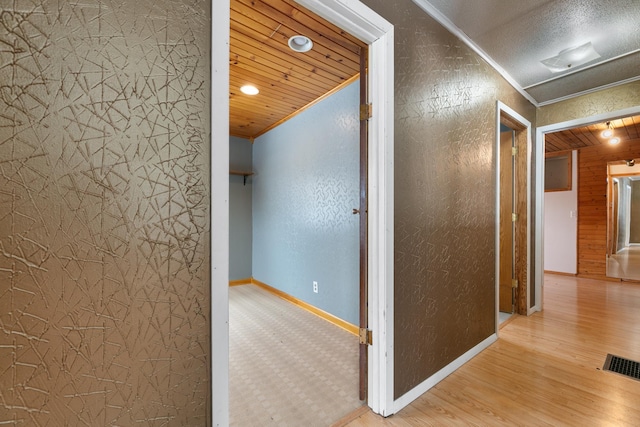 hallway featuring visible vents, light wood-style floors, wood ceiling, and crown molding