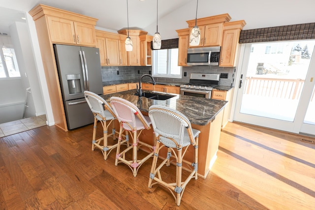 kitchen with decorative light fixtures, sink, dark stone counters, stainless steel appliances, and a center island with sink